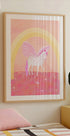 um pôster emoldurado de um unicórnio com um esquema de cores rosa e branco, contra um fundo rosa e amarelo com um arco de arco-íris.