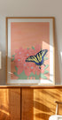 uma pintura emoldurada de uma borboleta em uma flor rosa, exibida em um armário ou prateleira de madeira.