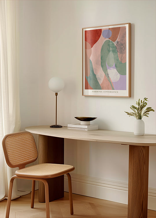 um espaço de trabalho minimalista com uma mesa de madeira, uma cadeira de tecido, uma luminária e uma pintura abstrata emoldurada na parede.
