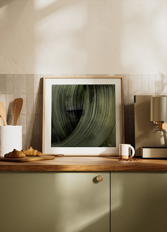 uma fotografia emoldurada de uma folha verde em um balcão de cozinha, com uma cafeteira e outros itens de cozinha visíveis ao fundo.