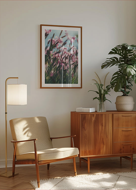 uma aconchegante sala de estar com armário de madeira, poltrona bege, quadro com flores cor de rosa e um vaso de planta.