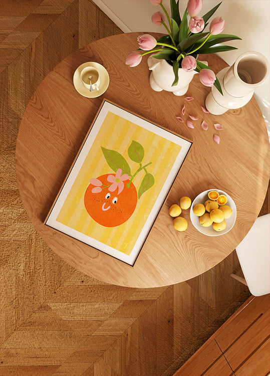 uma mesa de madeira com uma imagem emoldurada de uma laranja, uma tigela de limões, um vaso de tulipas cor de rosa e uma vela.