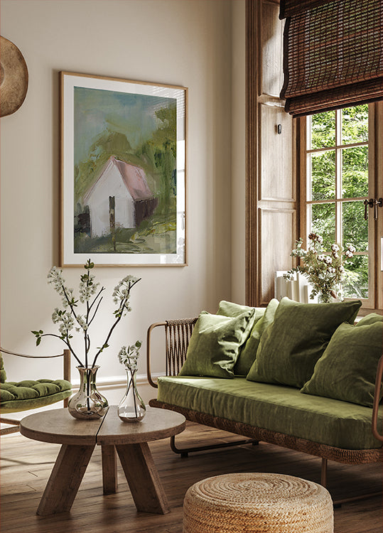 uma aconchegante sala de estar com uma grande janela, um sofá verde, uma mesa de centro de madeira e uma pintura emoldurada de uma casa.