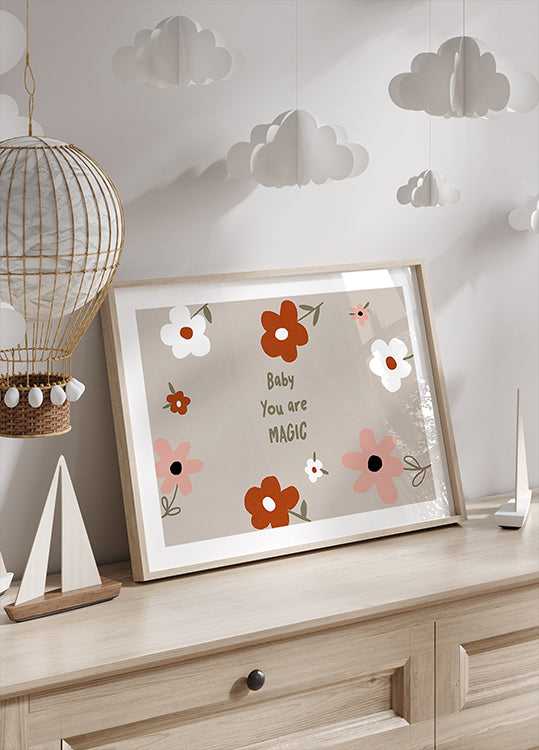 Uma estampa emoldurada com desenho floral e o texto "Baby You are Magic" é exposta em uma cômoda de madeira, com uma lanterna de papel decorativa pendurada acima dela.